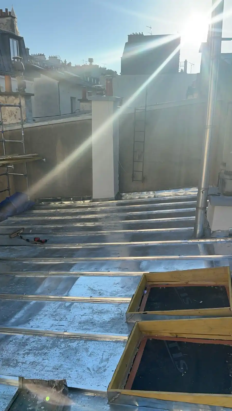 A photo of a sunlit rooftop under construction with metal roofing panels, scaffolding, and tools, overlaid with the text…