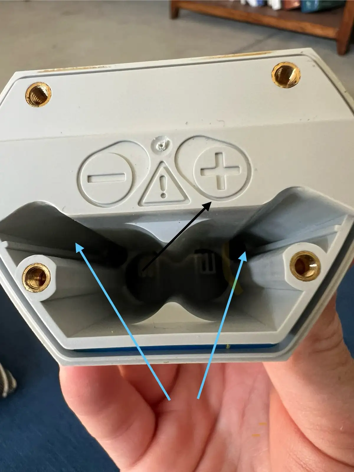 a close-up photo shows the underside of a white plastic device with a battery compartment. The compartment has embossed…