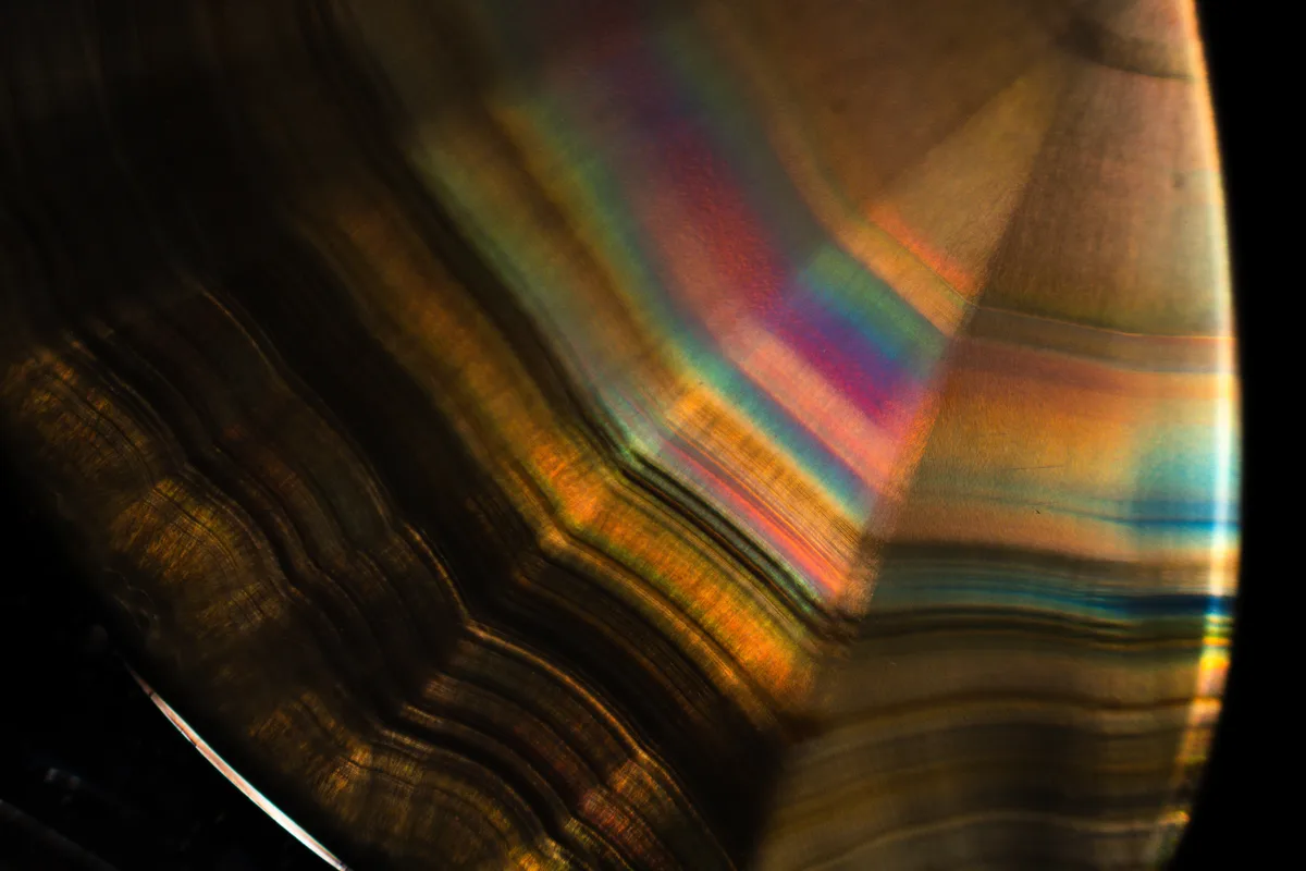 A close-up photo of a polished agate slice showing dark, wavy bands with iridescent rainbow colors reflecting off its…