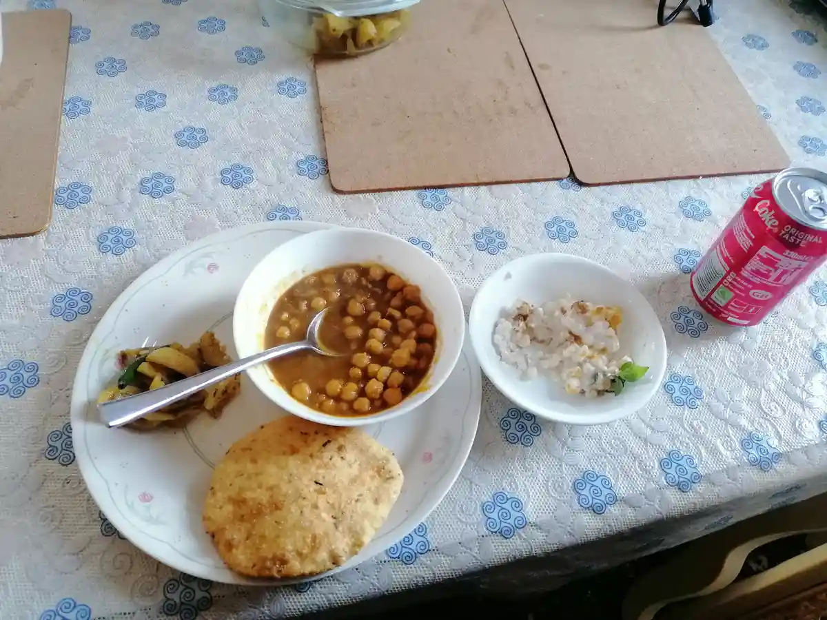 A plate of Indian-style food including chickpea curry, rice, and roti sits on a patterned tablecloth next to a can of…