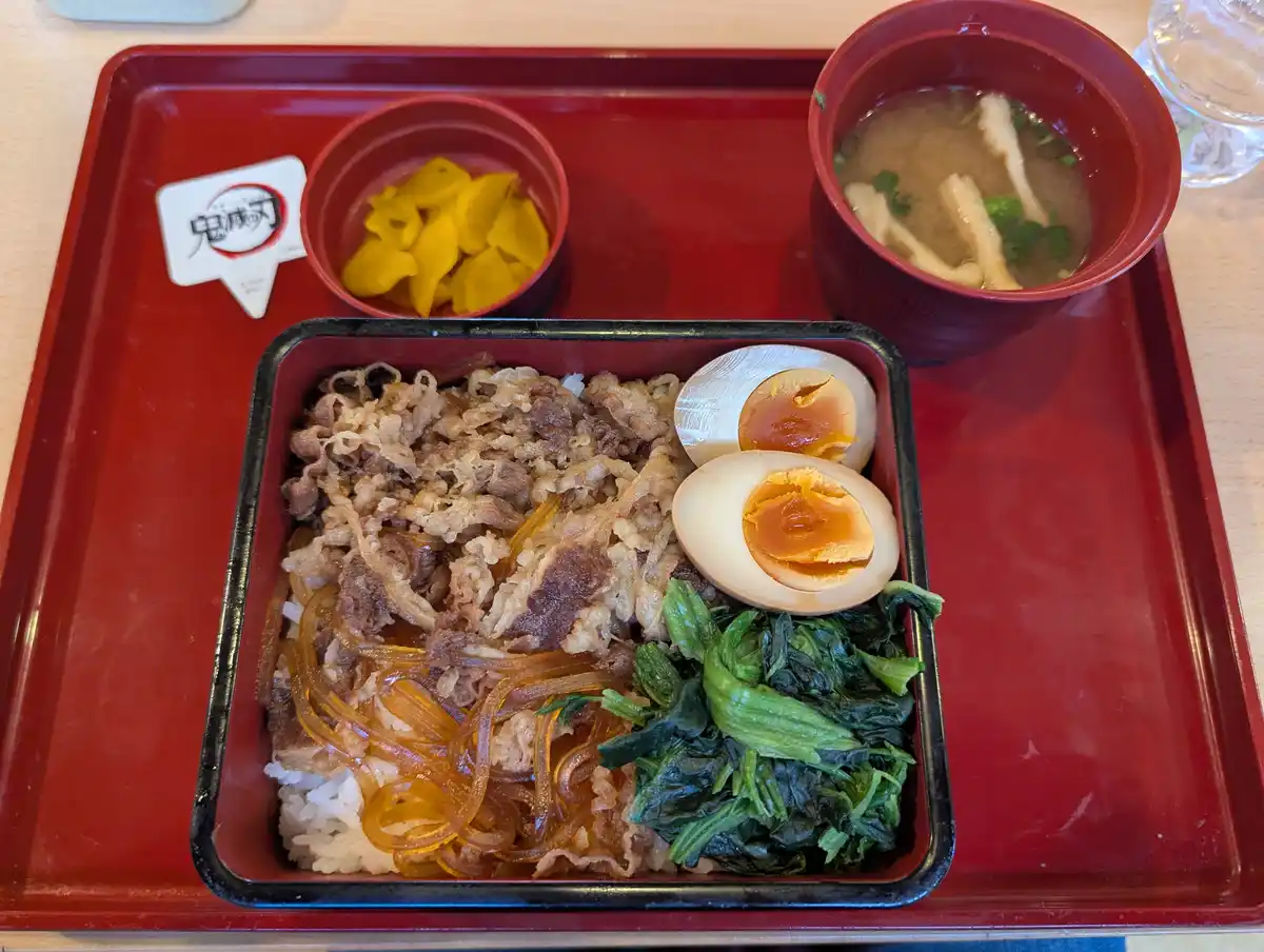 a japanese gyoza beef bowl with rice, shredded beef, translucent noodles, spinach, and a soft-boiled egg, served with miso…