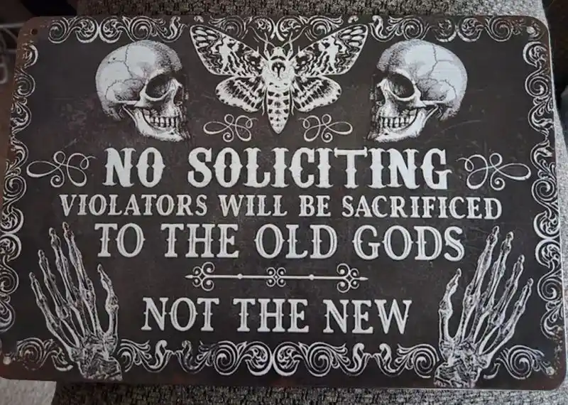A dark, ornate metal sign features two skulls flanking a large moth, with skeletal hands at the bottom. The text reads 'NO…