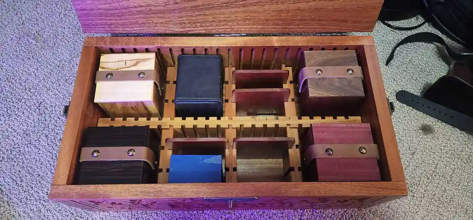 An open wooden box with a custom interior divider holds several small wooden and leather-bound boxes, some empty, arranged…
