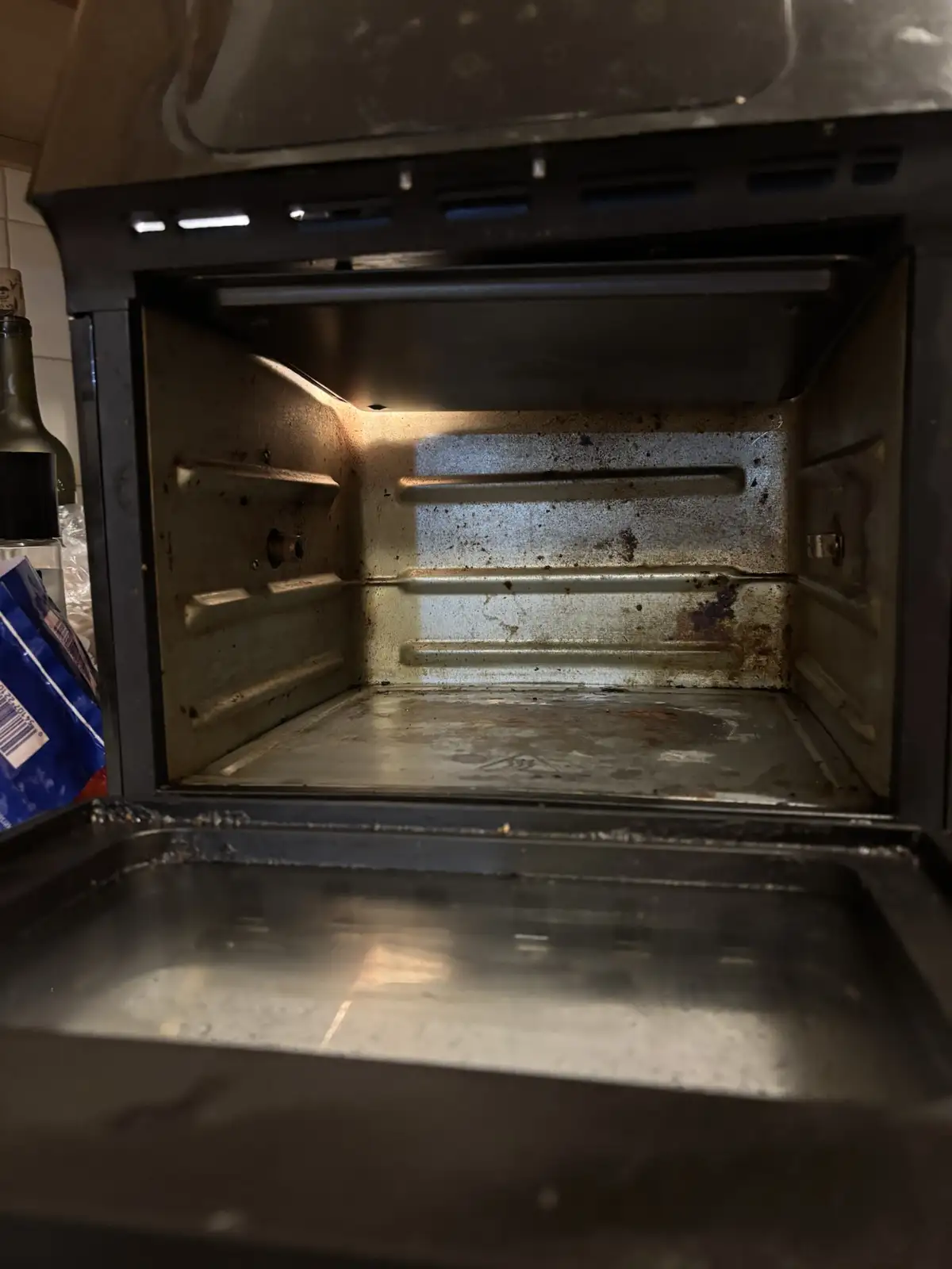 A close-up photo shows the inside of a dirty, grimy oven with visible grease and baked-on residue on its walls and racks…