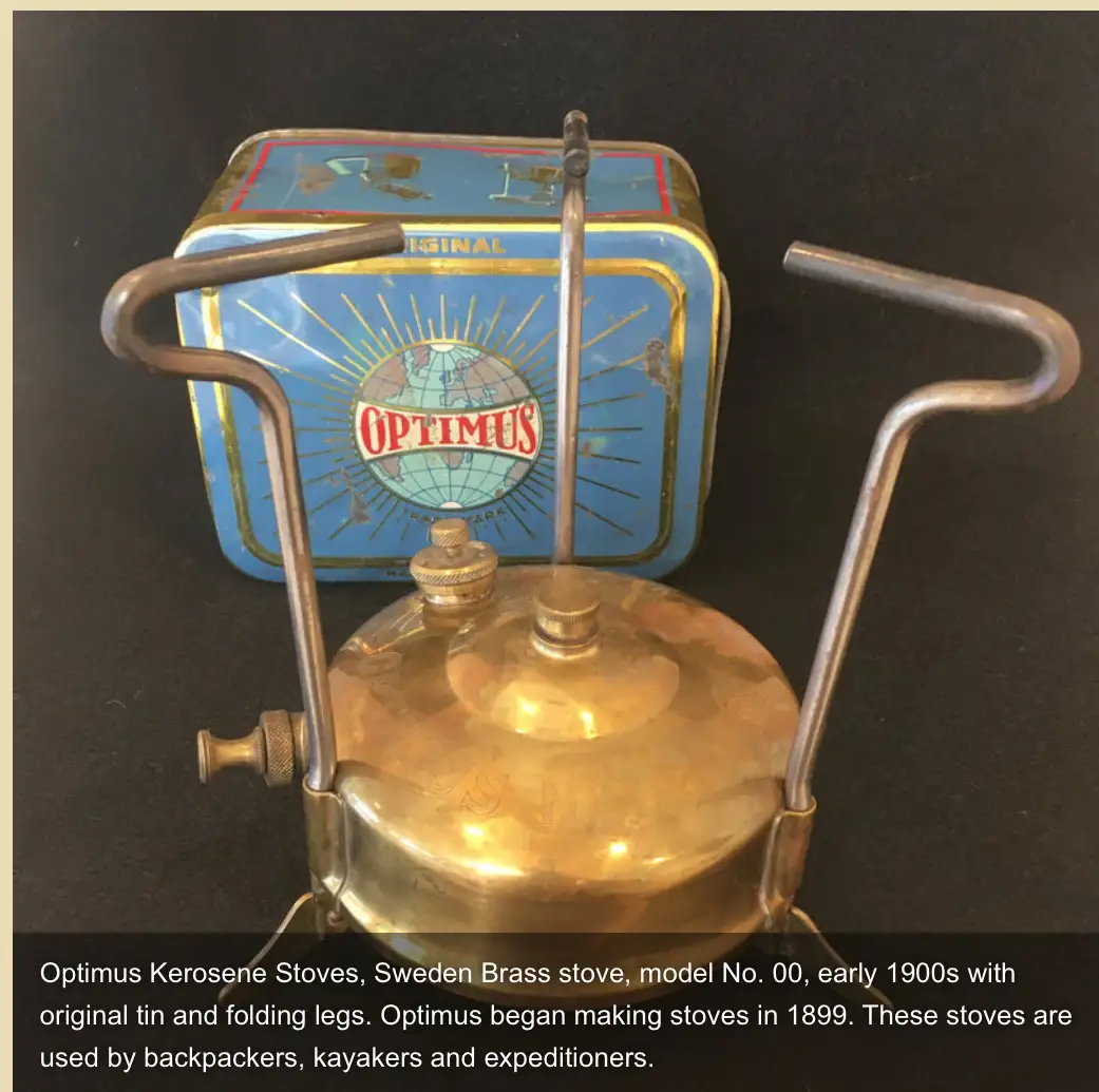 A vintage brass Optimus kerosene stove with folding legs sits in front of its original blue tin, which features a globe logo…