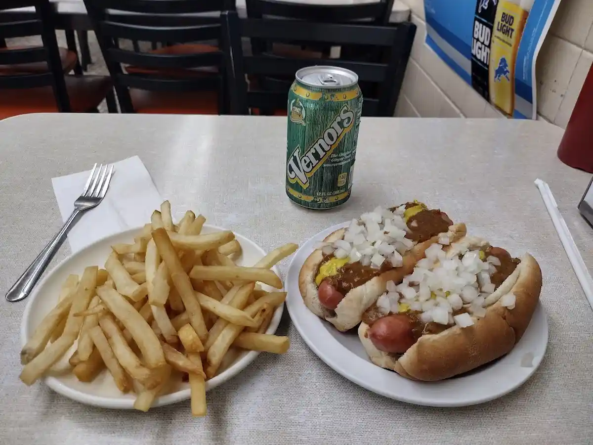 A photo of a meal featuring two chili dogs topped with onions and mustard, a side of french fries, and a can of Vernors soda…