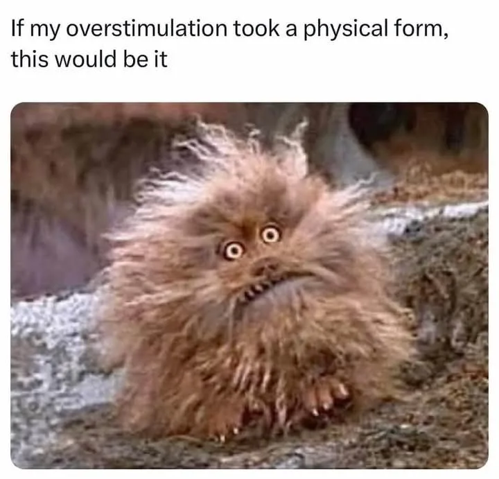 A furry, brown, disheveled creature with wide, startled eyes and a grimacing mouth sits on a rocky surface. The overlaid…