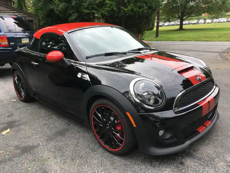 A black Mini Cooper with a red roof, side mirrors, and racing stripes parked in a lot. The overlaid text reads 'i'm not a…
