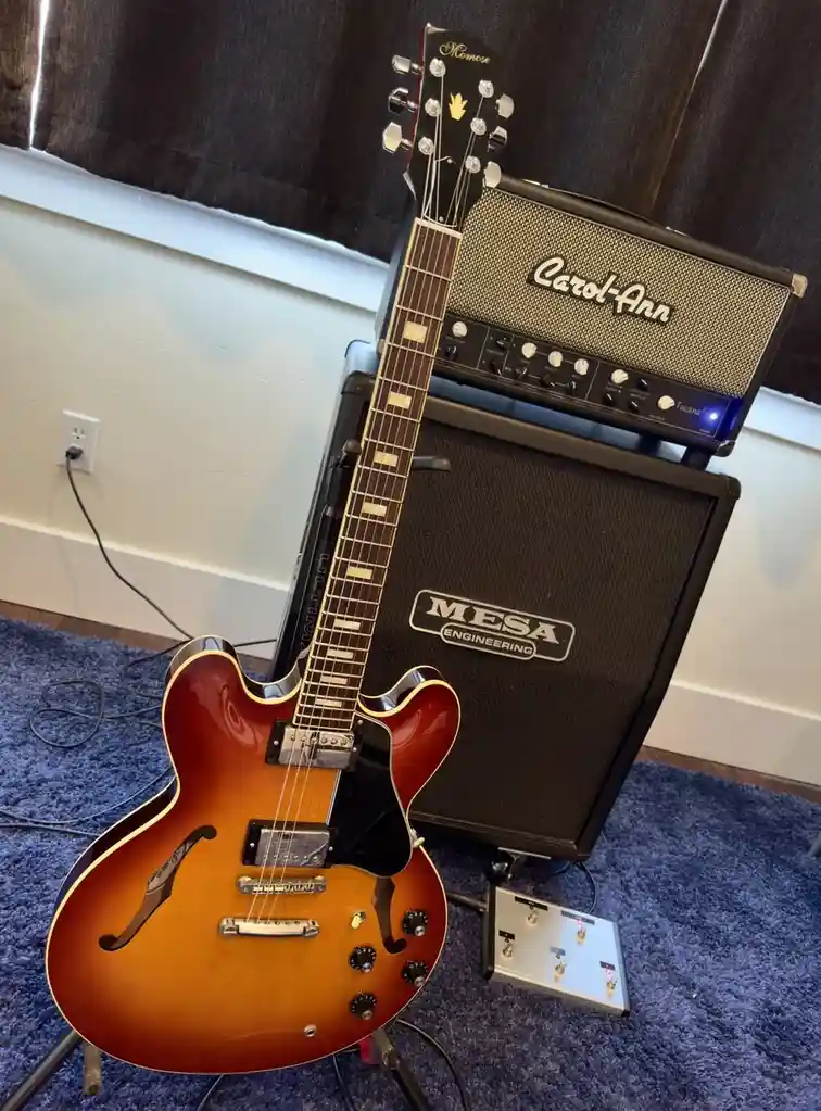 A sunburst-finish electric guitar, branded 'Memose', leans against a Mesa Engineering guitar amp stack topped with a…