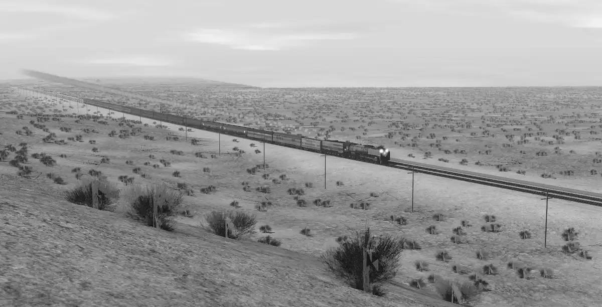 A black-and-white image shows a long train traveling across a vast, flat, arid landscape with sparse vegetation and power…