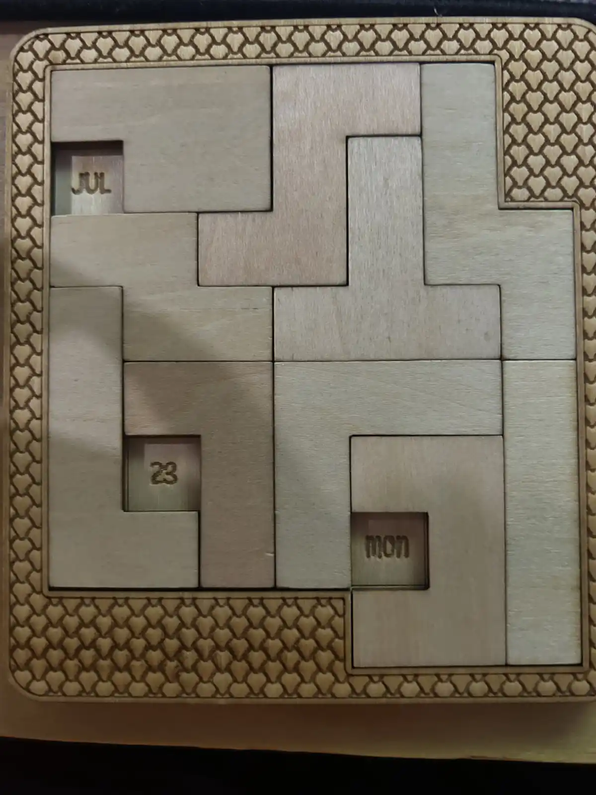 A wooden calendar puzzle with interlocking pieces, showing the month 'JUL', the date '23', and the day 'mon' in separate…