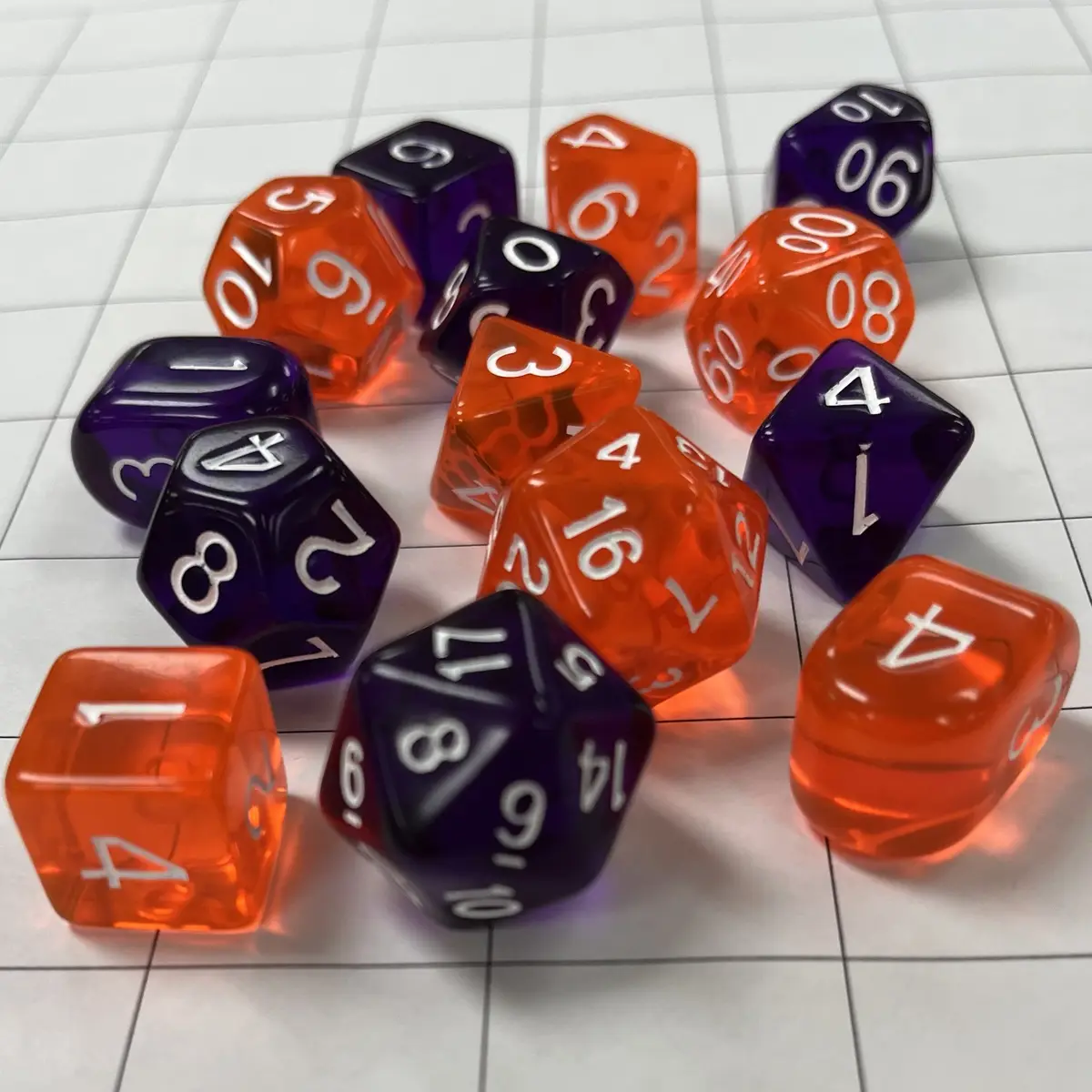 A collection of translucent orange and opaque purple polyhedral dice with white numbers are scattered on a white tiled…
