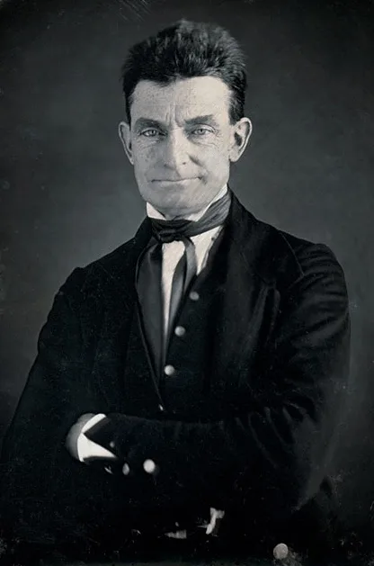A vintage black-and-white portrait of a man in a formal suit with arms crossed, looking directly at the camera with a subtle…