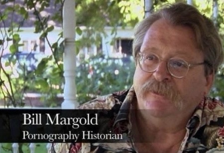 A man with glasses and a mustache, wearing a patterned shirt, is shown in an outdoor setting with foliage and white pillars…