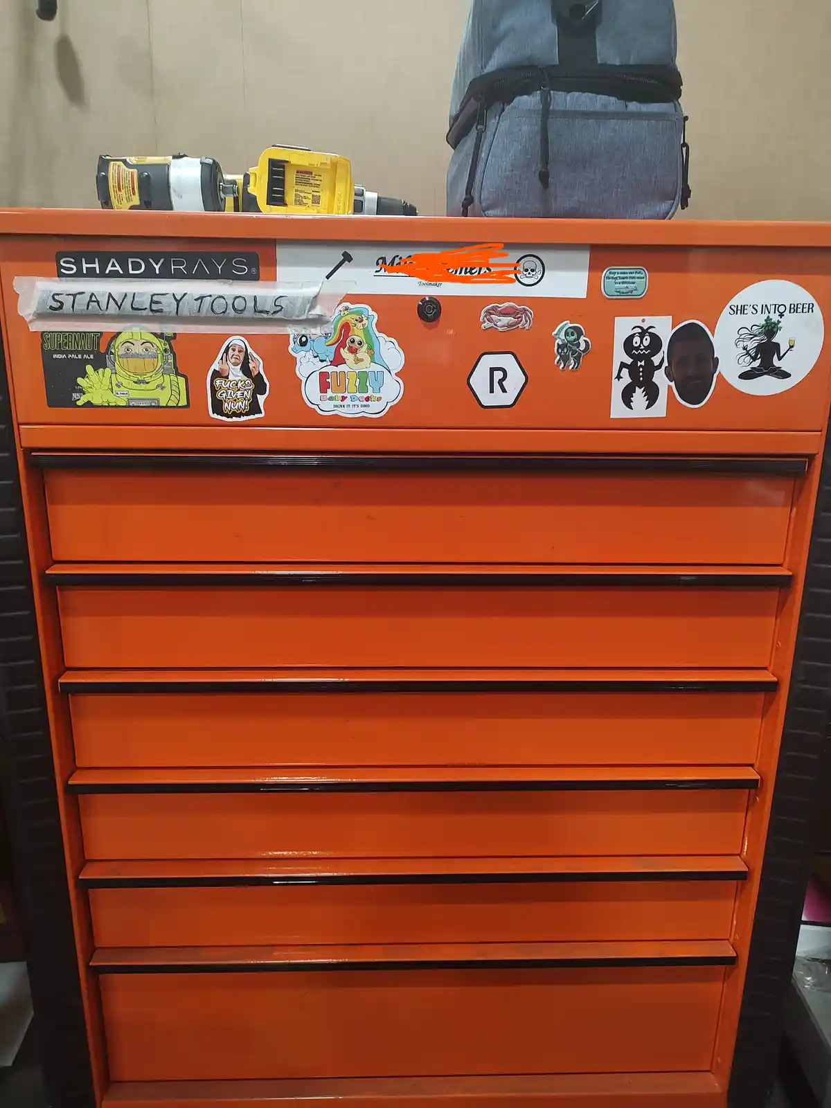 An orange Stanley tools chest covered in various stickers including 'She's Into Beer', a nun, fuzzy baby ducks, and a crab…