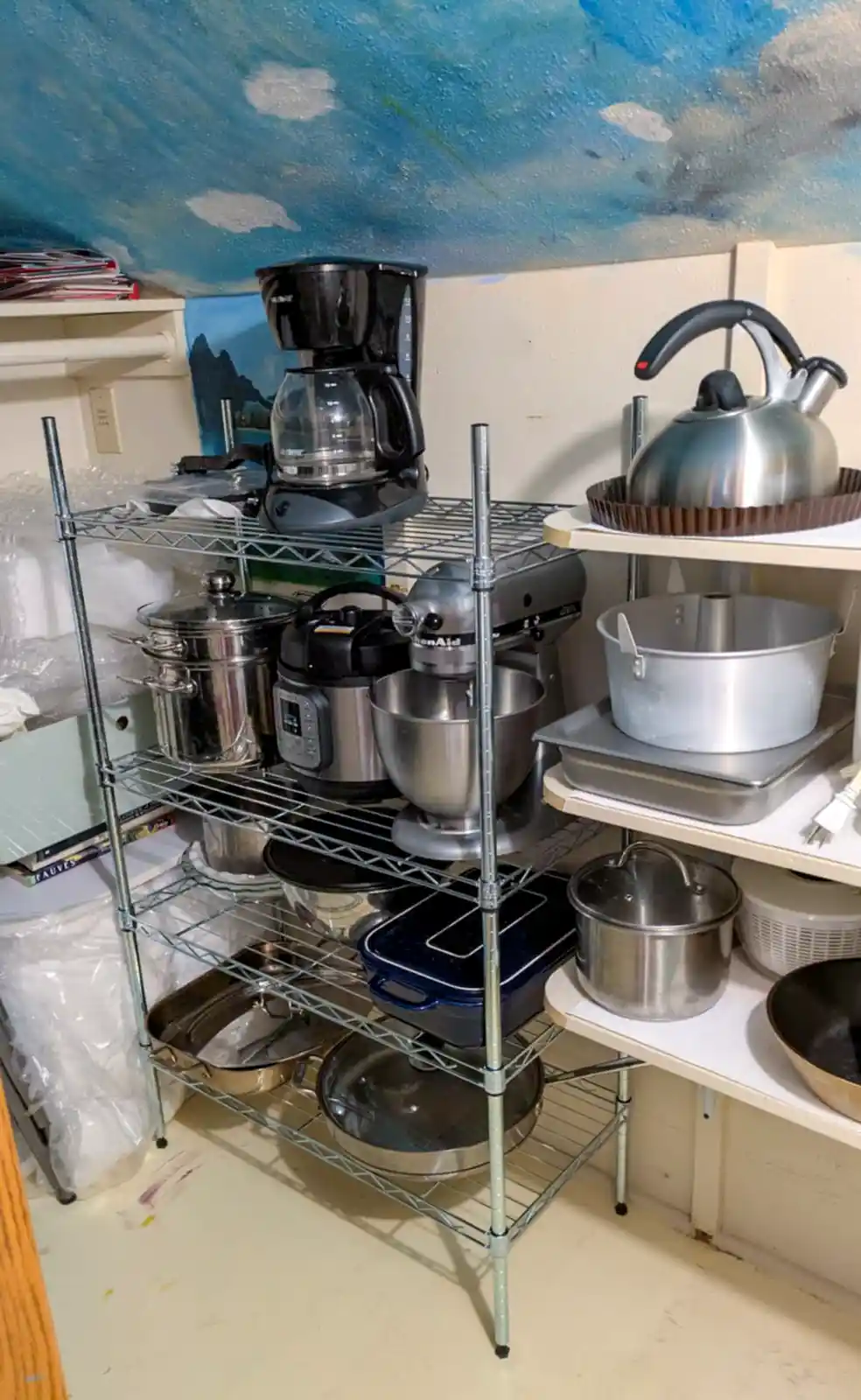 A cluttered kitchen corner with metal shelving units holding various appliances and cookware, including a coffee maker…