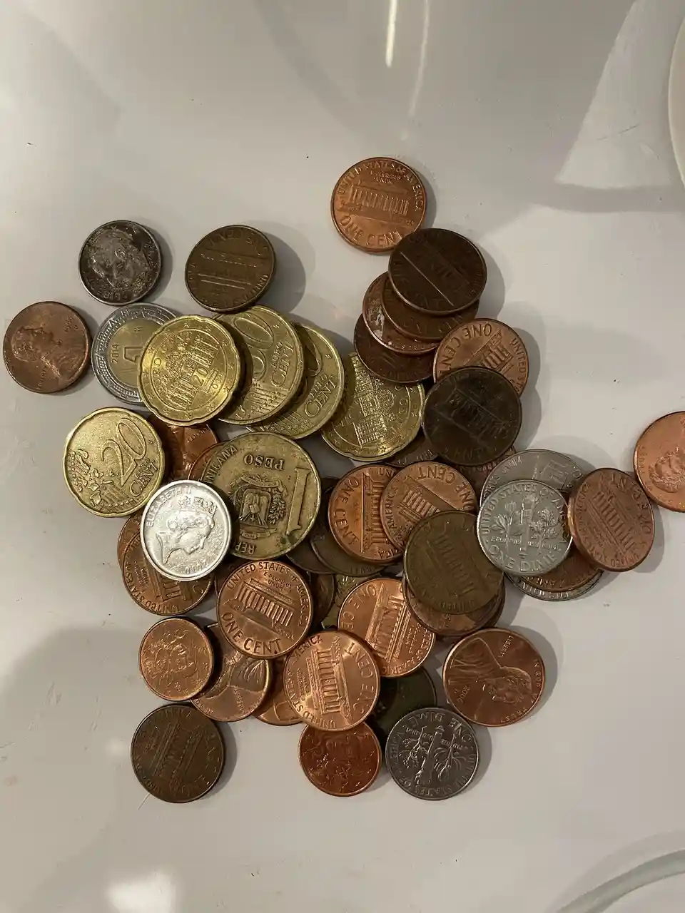 A pile of various coins, mostly U.S. pennies and dimes, along with some foreign coins like a 20 cent piece and a 1 peso…