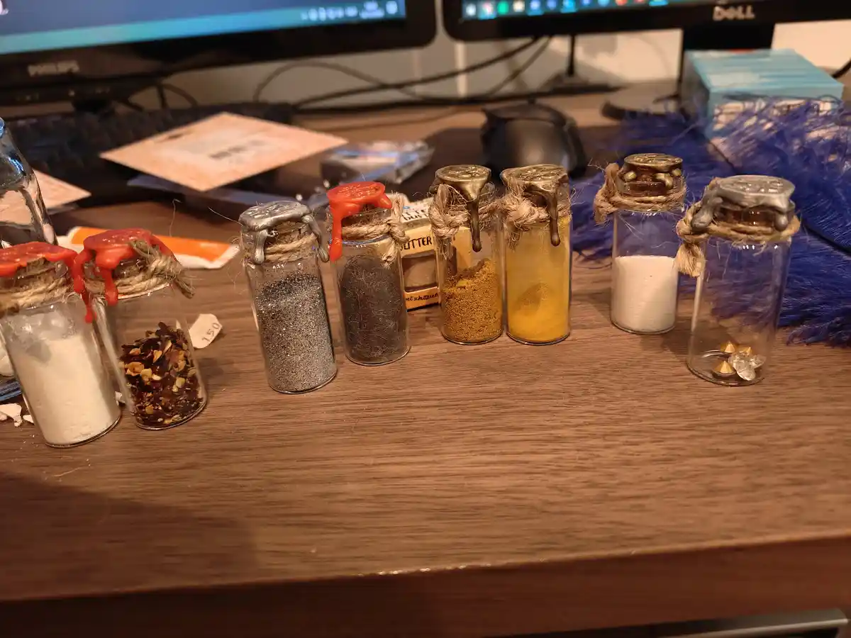 A row of small glass vials on a wooden desk, each sealed with wax and twine, contain various kitchen ingredients like salt…