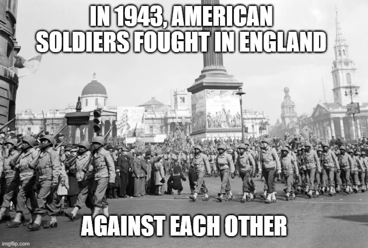 A black-and-white historical photo shows American soldiers in uniform marching in formation down a wide city street, flanked…