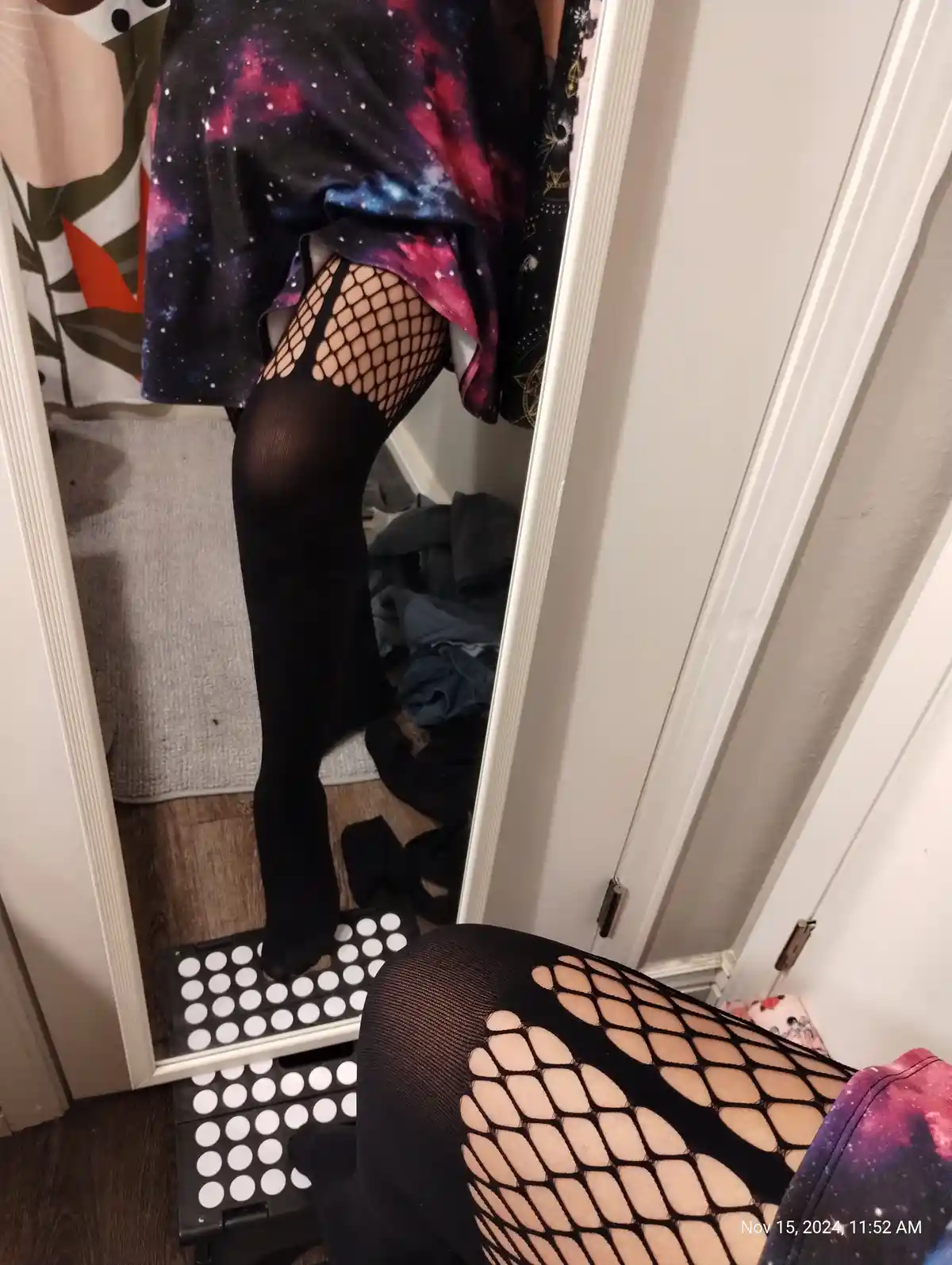 A person wearing black fishnet stockings with a galaxy-print skirt stands on a black step stool with white circular…