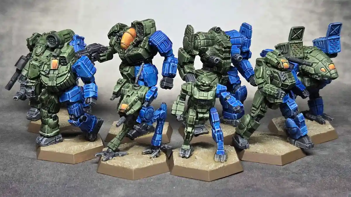 A collection of six painted miniature mechs, mostly green with blue accents, stand on hexagonal bases against a smoky…