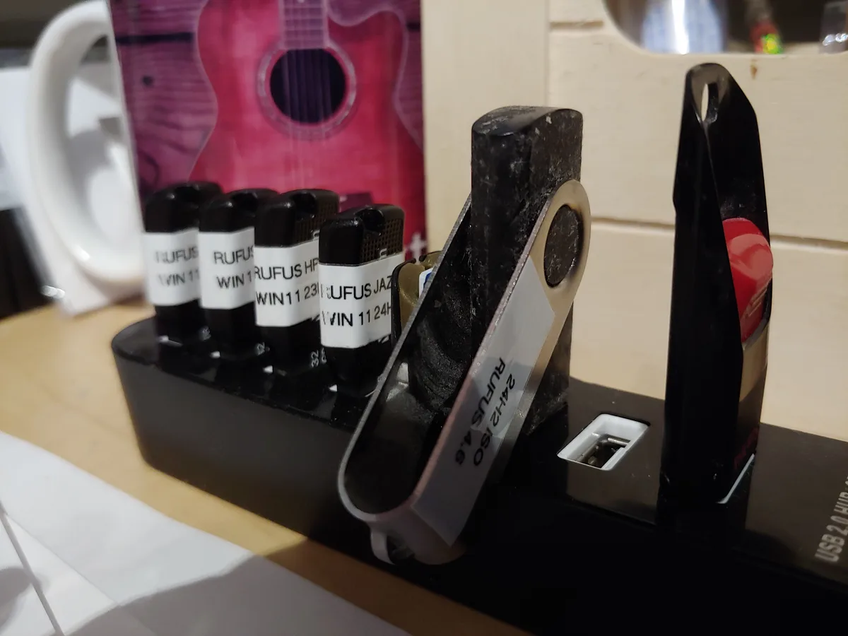 A close-up of several USB flash drives in a black holder, each labeled with 'RUFUS' and various Windows 11 version…