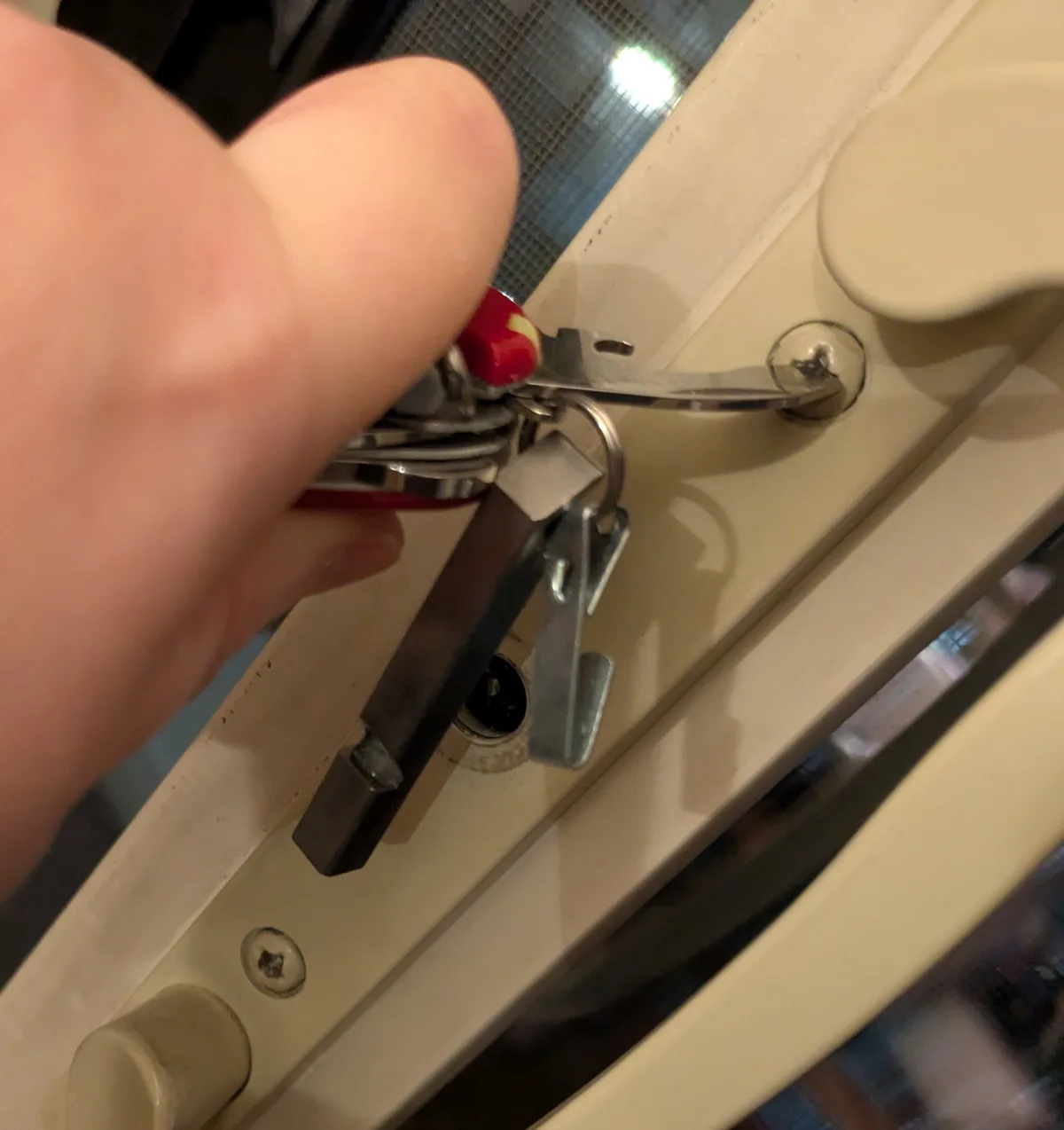 A close-up photo shows a person's hand holding a keychain that includes a screwdriver, which is being inserted into a screw…