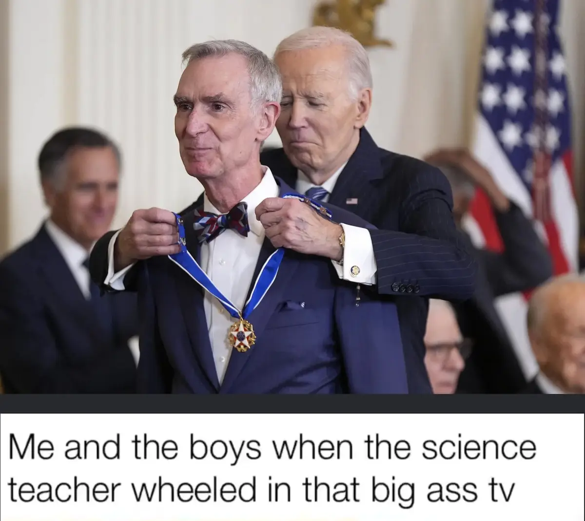 A man in a suit and bowtie stands as another man places a large medal around his neck in a formal setting with an American…