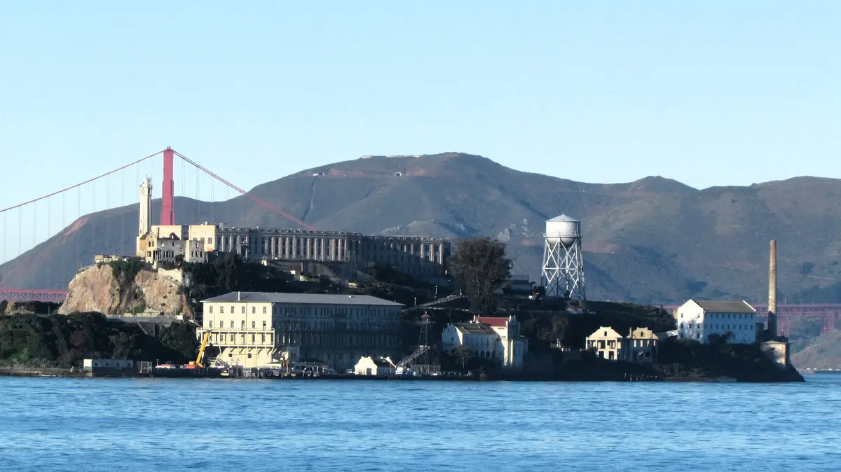 A scenic view of Alcatraz Island in San Francisco Bay, featuring its historic prison buildings, a water tower, and a…