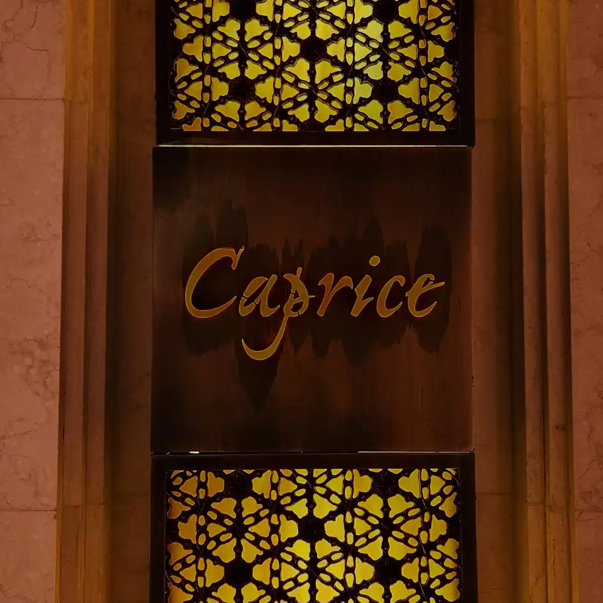A close-up of an ornate, dark wooden door panel with the word 'Caprice' in elegant gold cursive lettering, flanked by two…