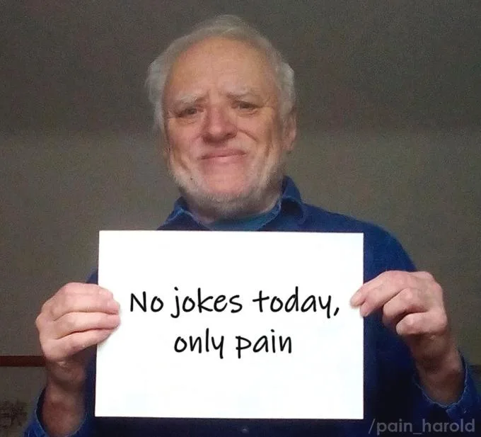 An older man with white hair and a beard, wearing a blue shirt, holds a white sign that reads 'No jokes today, only pain'…