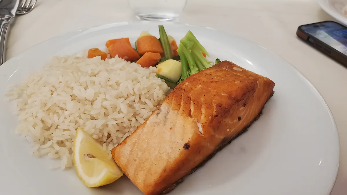 A plate of food featuring a grilled salmon fillet, white rice, mixed steamed vegetables including carrots and broccoli, and…