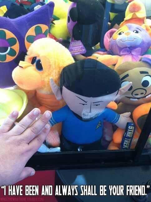 A hand reaches toward a plush toy of Spock from Star Trek, surrounded by other colorful stuffed animals in a claw machine…
