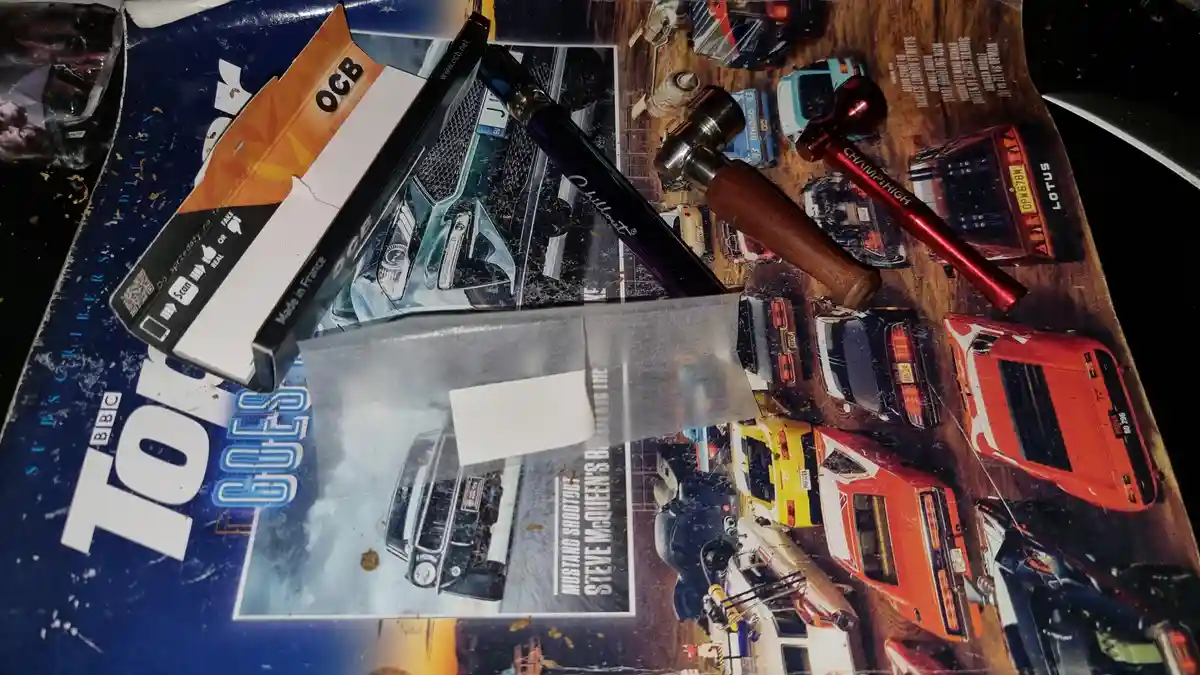 A close-up photo shows a 'Top Gear' magazine cover with various car images, overlaid with a pack of OCB cigarettes, a black…