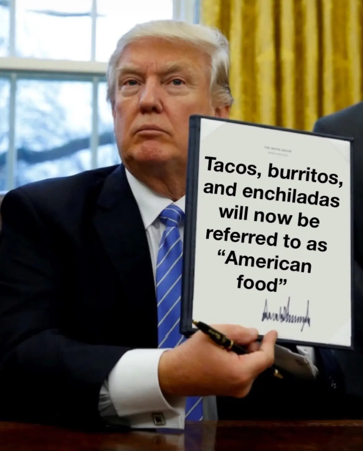 A man in a dark suit and blue striped tie sits at a desk holding a framed document that reads 'Tacos, burritos, and…