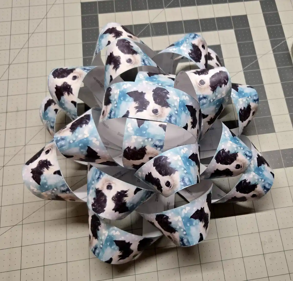 A large, elaborate bow made from ribbon printed with repeated images of a black and white border collie's face against a…