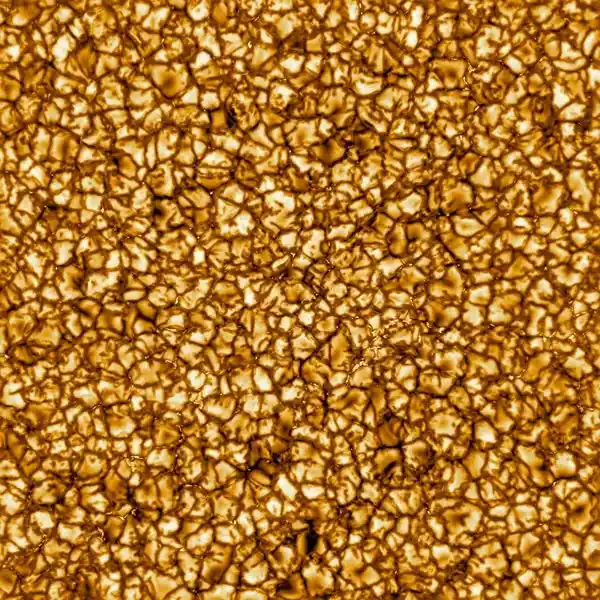 a close-up image of the sun's surface showing a granular, golden-yellow texture with bright, irregular cells and darker…
