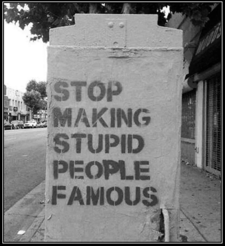 A black-and-white photo shows a concrete utility box on a city sidewalk with bold, stenciled text reading 'STOP MAKING…