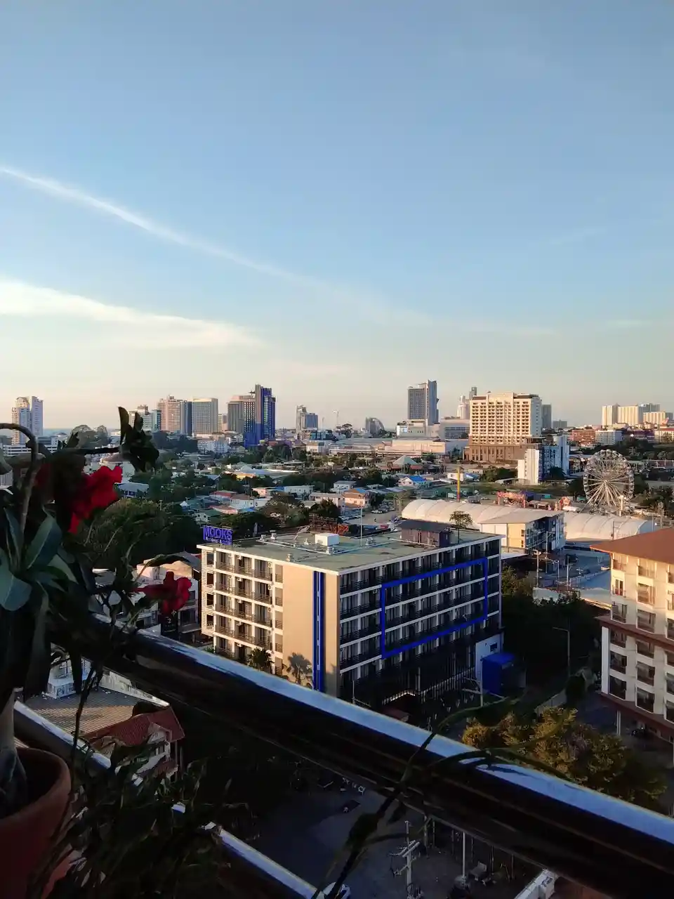 A scenic cityscape viewed from a balcony, featuring a clear blue sky, distant skyscrapers, and a visible Ferris wheel. In…