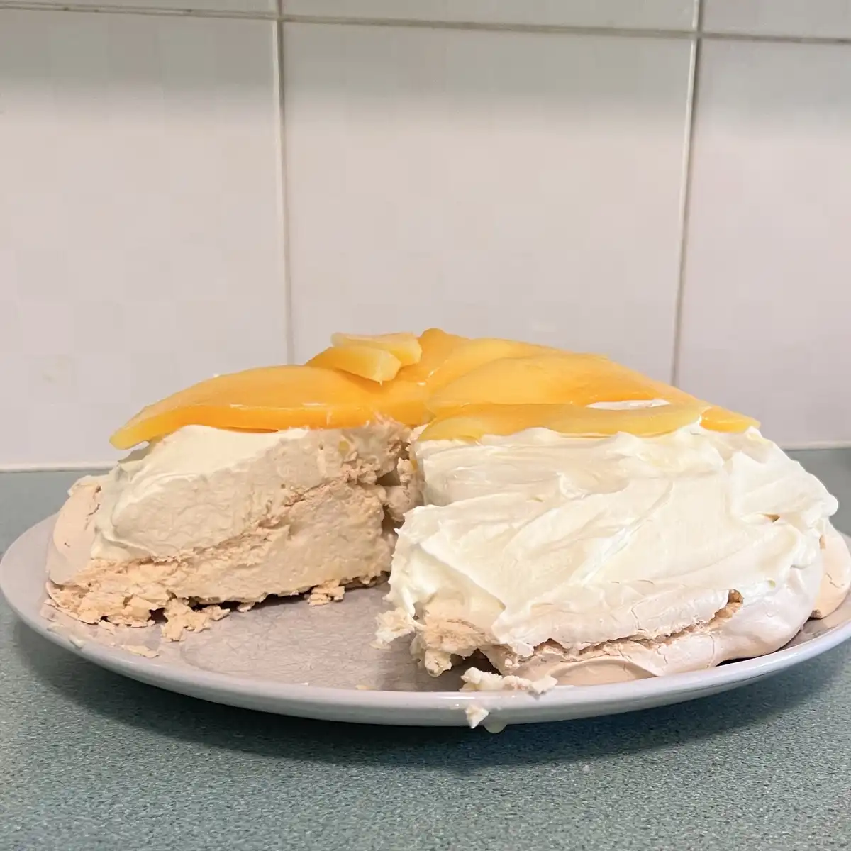 A partially eaten pavlova-style dessert with whipped cream and candied orange slices sits on a plate, with a large slice…