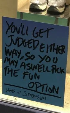 A handwritten note on blue paper taped to a glass surface, likely a door or window, with a pair of sneakers visible in the…
