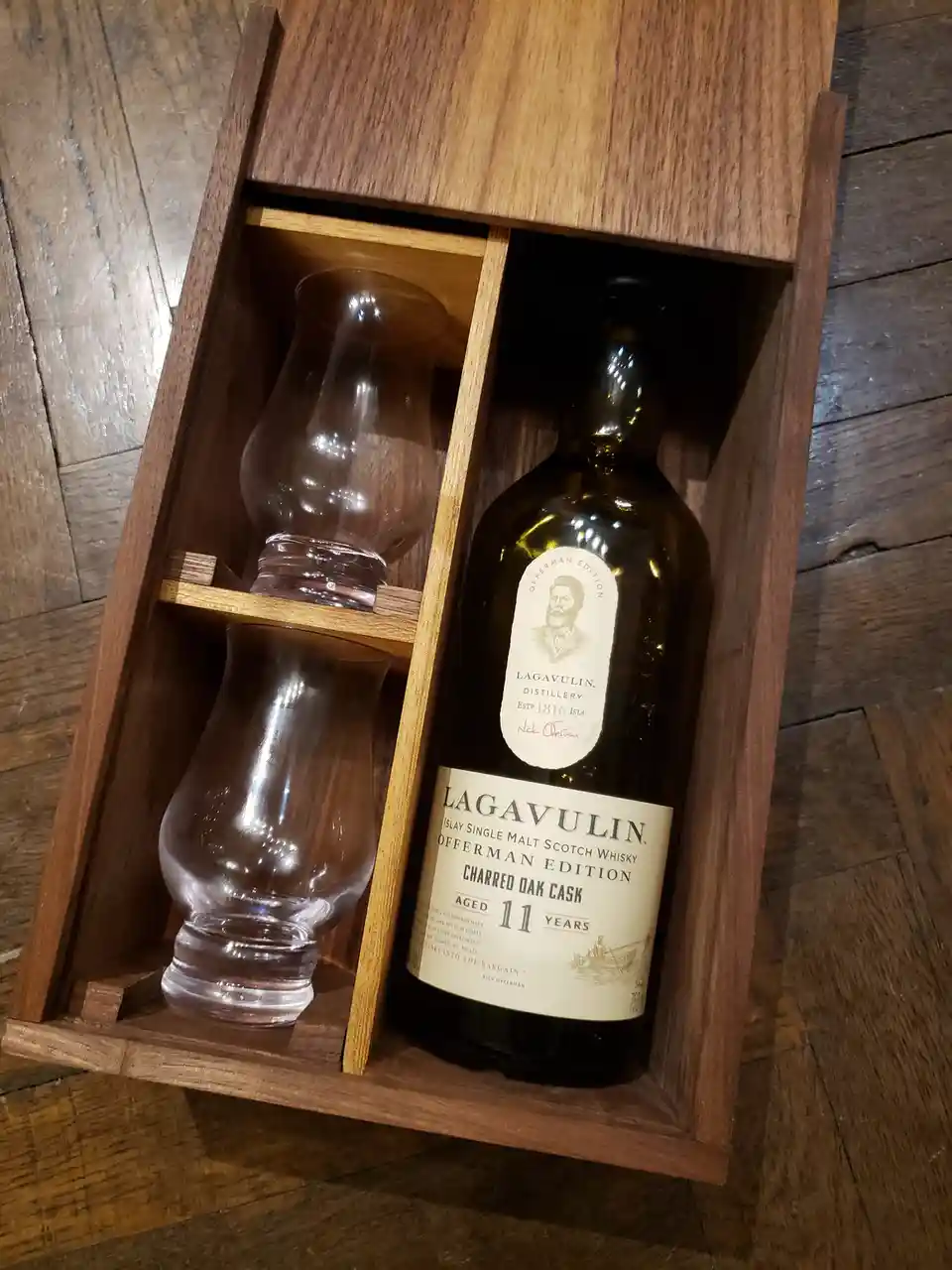 A wooden presentation box contains a bottle of Lagavulin 11-year-old Islay Single Malt Scotch Whisky, labeled 'Offerman…