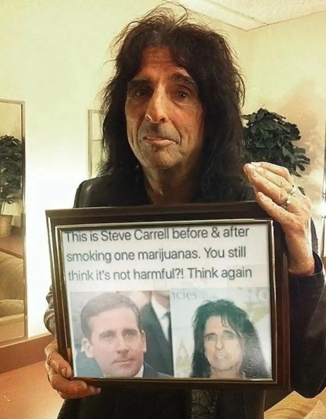 A man with long dark hair and a leather jacket holds a framed picture showing two photos side-by-side: one of Steve Carrell…