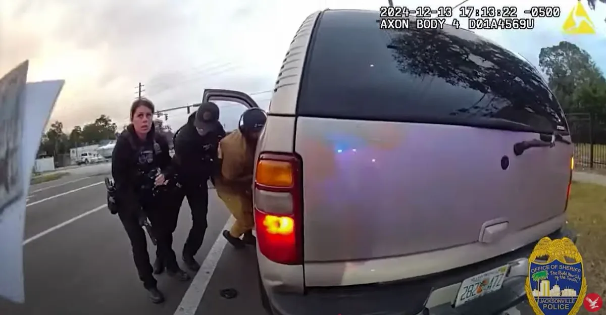 A bodycam video frame shows two police officers escorting a person in a yellow jumpsuit out of a silver van. The officer on…