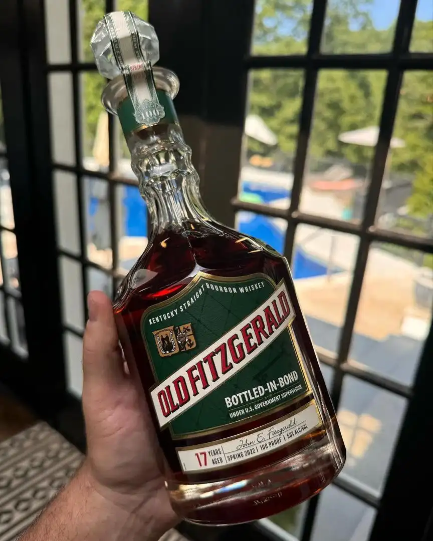 A hand holds a bottle of Old Fitzgerald 17-year-aged bourbon whiskey, labeled 'Bottled-in-Bond' and 'Under U.S. Government…