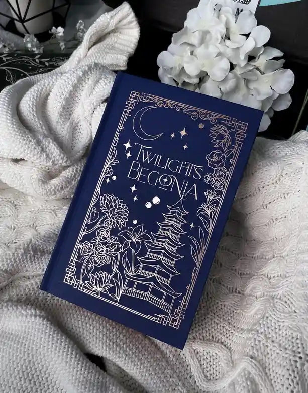 A dark blue book titled 'Twilight's Begonia' with gold foil designs of a crescent moon, stars, a pagoda, and various flowers…