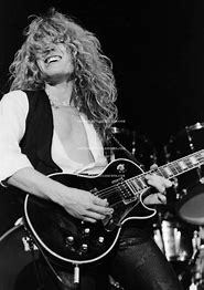 A black-and-white photo of a woman with long curly hair, wearing a white shirt and black vest, joyfully playing a black…
