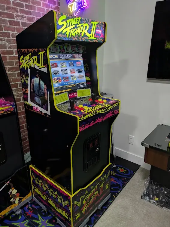 A vintage Street Fighter II arcade machine with bright neon artwork and a modern touchscreen interface, standing in a room…