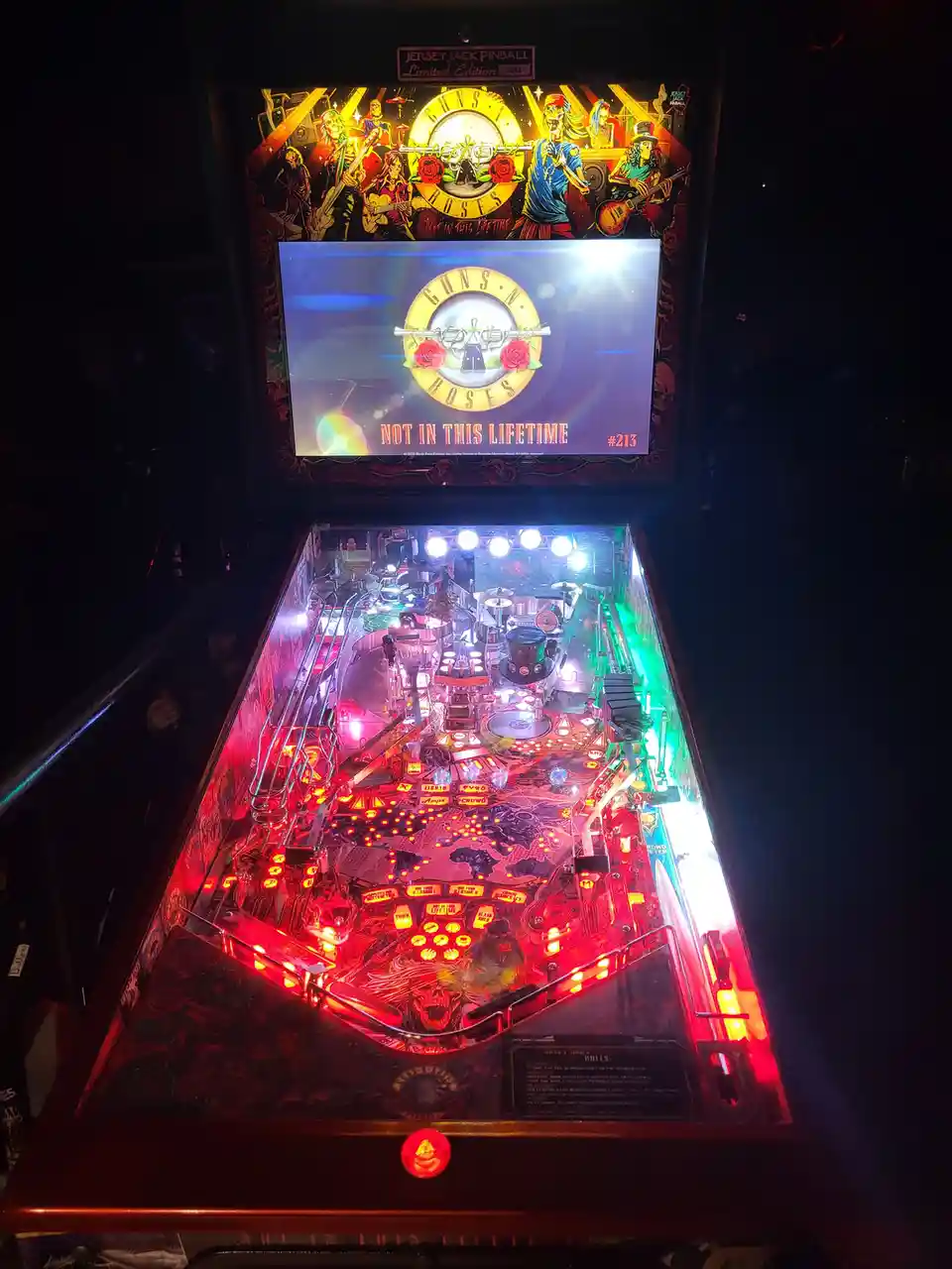 A brightly lit Guns N' Roses themed pinball machine by Jersey Jack Pinball, featuring the band's logo and artwork. The…