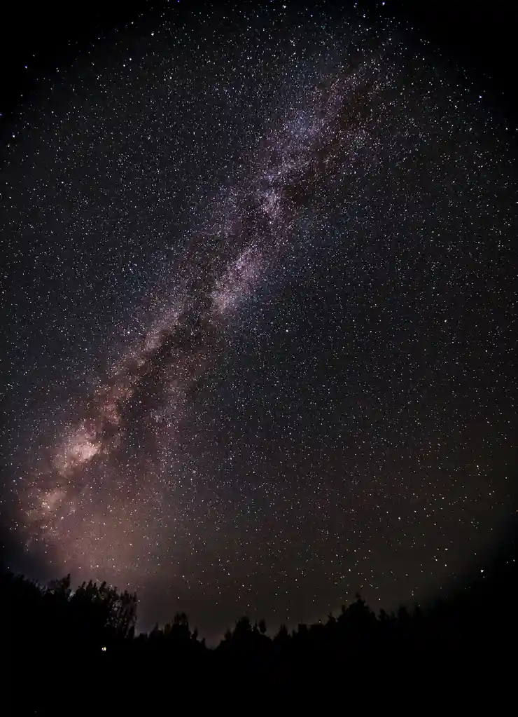 A stunning night sky photograph showing the Milky Way galaxy as a bright, dense band of stars and cosmic dust stretching…